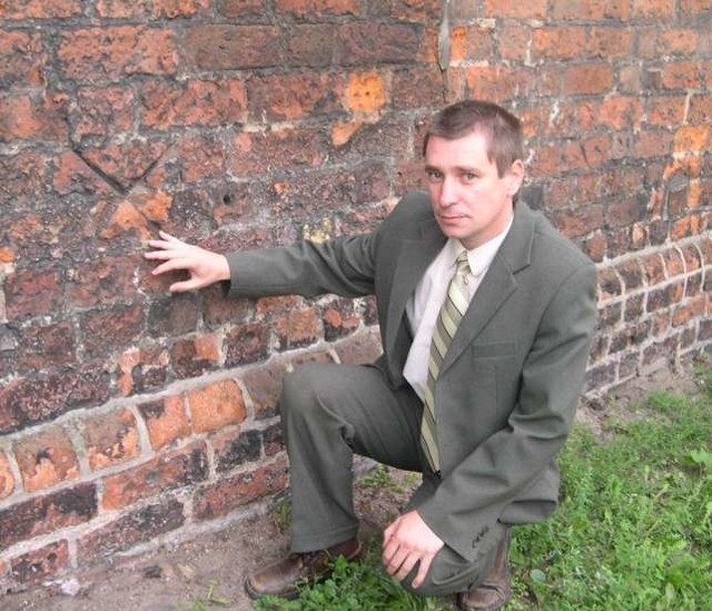 Maciej Tomaszczyk, sekretarz gminy pokazuje dziurki w murze.