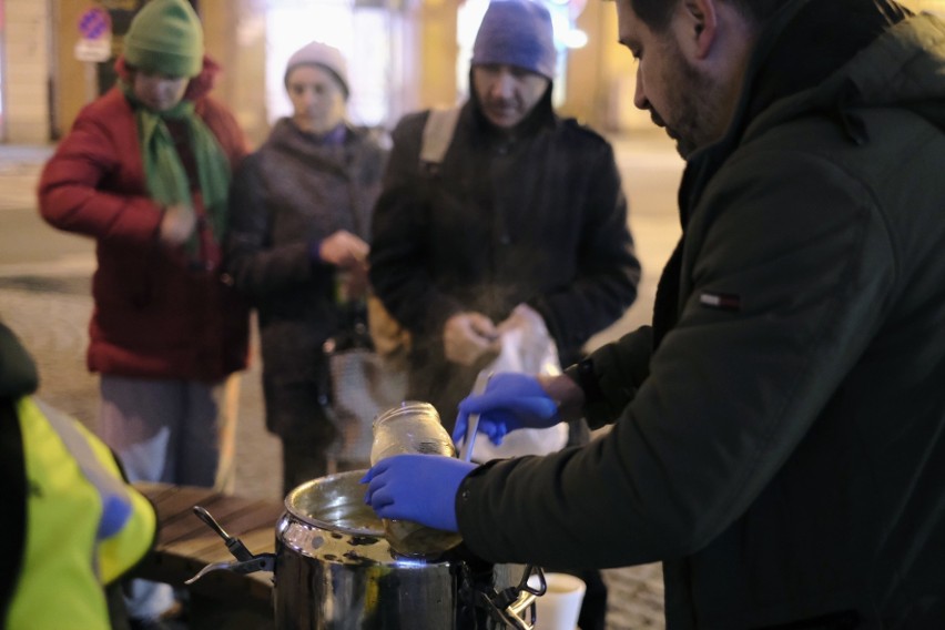 Wolontariusze częstują ciepłą zupą wegańską w oświetlonym,...