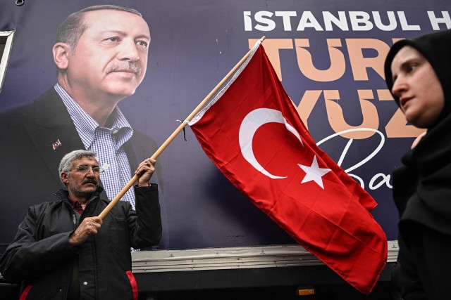 12 maja 2023 roku, Stambuł: zwolennik Erdogana pozuje z flagą Turcji na tle banneru wyborczego prezydenta.