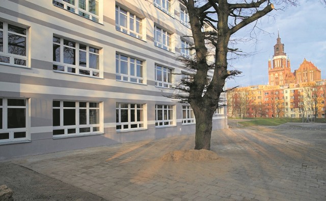 Po lewej stronie stonowana, nowa elewacja II Liceum Ogólnokształcącego, po prawej kolegiata wyglądająca zza dopasowanych kolorystycznie bloków przy ulicy Krzywoustego