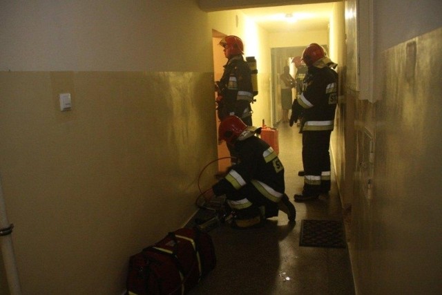 Strażacy wchodzą do zadymionego mieszkania.