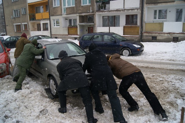 Kilku dorosłych mężczyzn jest potrzebnych, żeby wypchać samochód ze zwałów śniegu.