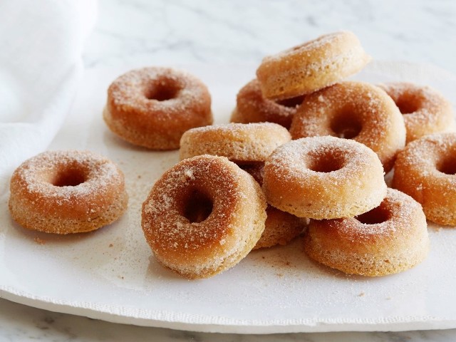 Jeżeli jeść pączki w Tłusty Czwartek, to na bogato! Niech będą wyśmienite, puszyste, aromatyczne i warte każdej swojej kalorii. Oto przepisy od prawdziwych mistrzów kuchni Polsat Food Network!„Bosonoga Contessa” Ina Garten dzieli się błyskawicznym przepisem na wykwintne cynamonowe donaty, które można przygotować nawet w ostatniej chwili. „Kobieta na Dzikim Zachodzie”, królowa kowbojskiej kuchni Ree Drummond proponuje tradycyjne, drożdżowe pączki z pysznym lukrem. Cynamonowe donaty z piekarnika Przepis: Ina GartenPoziom trudności: łatwy Przygotowanie: 15 minutOczekiwanie: 5 minut Pieczenie: 15 minutLiczba: 12 pączkówCałkowity czas: 35 minSkładniki:- 2 szklanki mąki- 1 1/2 szklanki cukru- 2 łyżeczki proszku do pieczenia- 1 łyżeczka mielonego cynamonu- 1/2 łyżeczki gałki muszkatołowej- 1/2 łyżeczki soli - 1 bardzo duże jajko- 1 1/4 filiżanki mleka pełnotłustego- 2 łyżki masła, roztopionego- 2 łyżeczki czystego ekstraktu z wanilii	Posypka:- 8 łyżek masła- 1/2 szklanki cukru - 1/2 łyżeczki mielonego cynamonuPrzygotowanie: Rozgrzej piekarnik do 180°C. Przygotuj 2 blachy z formami do donatów. Jeżeli ich nie masz, możesz też użyć formy do muffinów. Nasmaruj je tłuszczem wewnątrz. Do dużej miski przesiej mąkę, cukier, proszek do pieczenia, cynamon, gałkę muszkatołową i sól. W drugiej, mniejszej misce wymieszaj roztrzepane jajko, mleko, roztopione masło i wanilię. Wymieszane mokre składniki wlej do miski z suchymi składnikami i wymieszaj je dokładnie razem, aż się połączą. Wlej porcje ciasta do foremek, wypełniając każdą w ok. ¾ wysokości. Wstaw do piekarnika i piecz przez ok. 17 minut lub do momentu, kiedy wetknięta w ciasto wykałaczka będzie czysta i sucha. Pozwól im ostygnąć przez 5 minut, po czym odwróć formę do góry nogami i ostrożnie wytrząśnij je na zewnątrz.Rozpuść 8 łyżek masła w rondelku albo misce. W drugiej misce przygotuj cukier wymieszany z cynamonem. Maczaj jedną stronę pączka w maśle, po czym dociśnij ją do cukru cynamonowego, aby się przykleił do mokrej powierzchni.