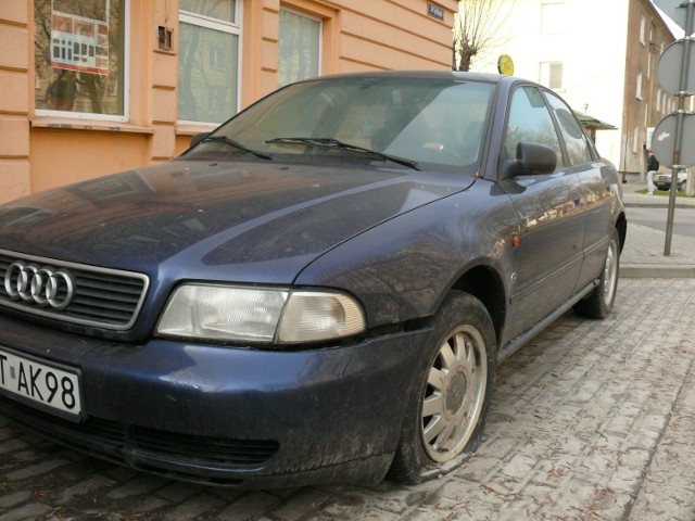 Audi z przebitymi oponami na parkingu.