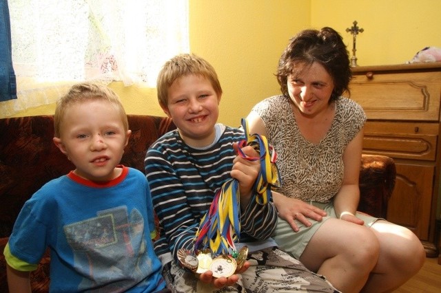 Daniel Przybyła, na zdjęciu z mamą Jadwigą i bratem Pawłem, prezentuje medale zdobyte na olimpiadach specjalnych.