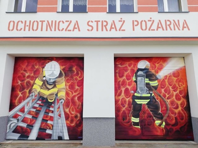 Na jednej bramie remizy - strażak wchodzący po drabinie, na drugiej bramie - strażak w ogniu