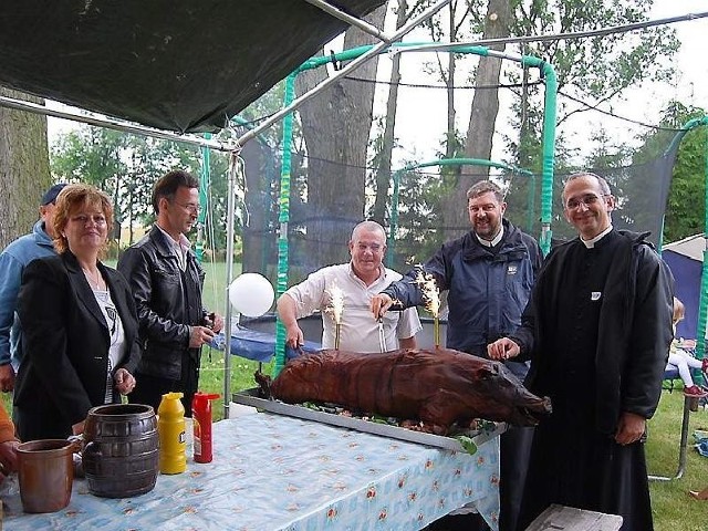 Ks. proboszcz Krzysztof Wojnowski w towarzystwie misjonarza ojca Grzegorza Lachowicza i Mirosława Boducha, prezesa Stowarzyszenia zapraszają do skosztowania prosiaka z rożna.