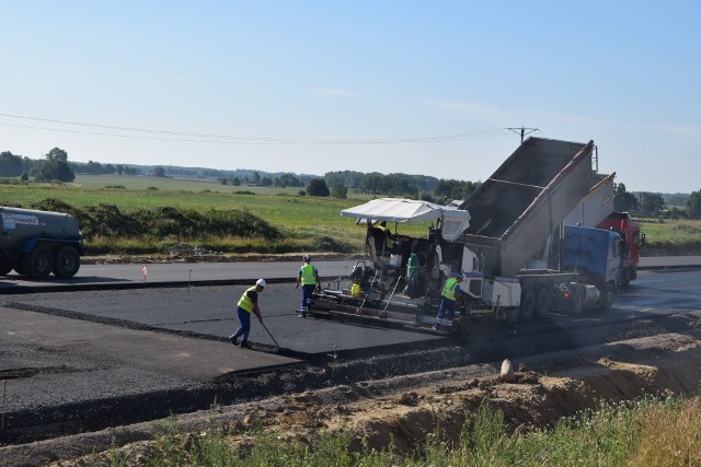 Na 800-metrowym odcinku obwodnicy Szczecinka na południe od miasta, koło Miękowa, pojawiły się walce drogowe. - Trwają prace związane z realizacją pierwszych odcinków bitumicznych na trasie głównej – informuje Mateusz Grzeszczuk, rzecznik prasowy Generalnej Dyrekcji Dróg Krajowych i Autostrad w Szczecinie. Na tym odcinku układana jest podbudowa bitumiczna, jak i również warstwa wiążąca. - Jest to tak zwany odcinek próbny, który służy również do weryfikacji prawidłowości wykonywanej nawierzchni, głownie składu mieszanki mineralno-asfaltowej – wyjaśnia Mateusz Grzeszczuk. Praca wre na całym, 120-kilometrowej obwodnicy Szczecinka. Mamy bowiem środek sezonu budowlanego. - W najbliższych tygodniach będą kontynuowane roboty związane z budową obiektów mostowych i realizacją robót drogowych – dodaje rzecznik. - oboty drogowe skupiają się na tym, aby finalizować roboty ziemne i doprowadzać kolejne odcinki do etapu wykonywania warstw konstrukcyjnych drogi. Obecne zaawansowanie finansowe budowy obwodnicy to przekracza już połowę wysokości kontraktu opiewającego na 322 miliony złotych. Są i gorsze wieści, bo obwodnicą raczej nie przejedziemy w kwietniu 2019, jak planowano. Kiedy trasa będzie gotowa? Na razie nie wiadomo. - Wykonawca złożył roszczenia dotyczące przesunięcia terminu na ukończenie zadania, roszczenia te są analizowane przez inżyniera kontraktu i GDDKiA – mówi Mateusz Grzeszczuk. - Ze wstępnych analiz wynika, iż nastąpi pewne przesunięcie czasu na ukończenie kontraktu w stosunku do pierwotnego terminu umownego. Po zakończeniu analiz i uzgodnieniu z wykonawcą treści zostanie zawarty stosowny aneks terminowy. Korzystający z objazdu w Budnie narzekają na wyboje na trasie ułożonej z betonowych płyt. – Mam nowy samochód, a już końcówki stabilizatora muszę wymieniać – mówi jeden z kierowców. – Ostatnio też o mało nie staranowała mnie ciężarówka wyjeżdżająca na złamanie karku z placu budowy. Dowiedziałem się, że kierowcy pracują ponoć na akord, więc bardzo się śpieszą, ale kosztem naszego bezpieczeństwa. - Objazd w Bugnie jest przejezdny, jego stan jest monitorowany i uszkodzenia nawierzchni są na bieżąco usuwane – komentuje rzecznik GDDKiA. - W ostatnim czasie nie trafiały do nas uwagi odnośnie stanu tego objazdu. Oczywiście objazd z płyt betonowych ten nie zapewnia takiego komfortu przejazdu jak równa nawierzchnia bitumiczna, kierowcy powinni w miejscach, w których są tymczasowe organizacje ruchu szczególną ostrożność.Szczecinek: Książka o historii Szczecinka