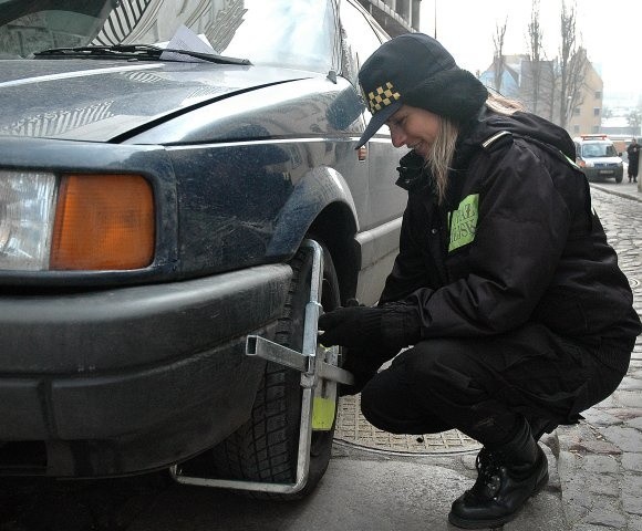 Strażniczka Kinga Lisewska zakłada kolejne blokady na kołach samochód, których kierowcy złamali przepisy parkując na ulicy Kuśnierskiej. Zdjęcie ich będzie kosztować 100 zł i 1 pkt. karny.