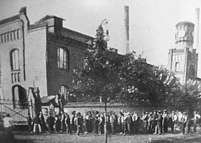 Robotnicy stojący przed bramą wejściową do zakładu. Zdjęcie zrobiono w 1910 roku.