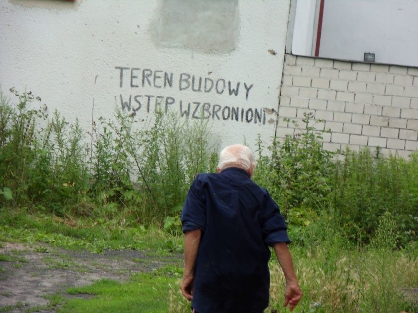 Teren w pobliżu budynków zarasta wysokimi chwastami.