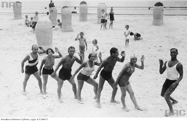 Kuracjusze podczas lekcji tańca na plaży prowadzonej przez czarnoskórego instruktora.