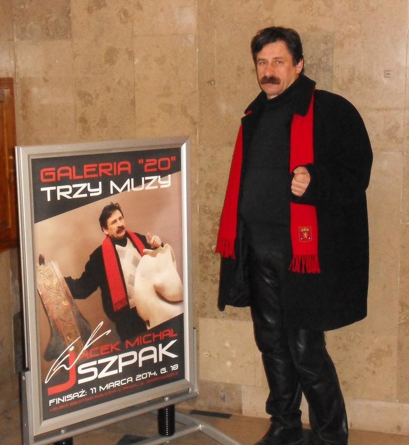 Jacek Michał Szpak przy plakacie wystawy.