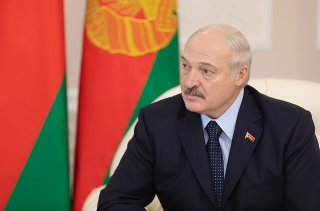 Aleksander Łukaszenko na tle obecnej flagi Białorusi.