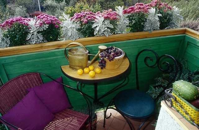 Przytulny balkonowy kącik. Na niewielkiej przestrzeni zmieścił się niewielki stolik i dwa krzesła. Otulony kwiatami balkon to idealne miejsce do wypoczynku.