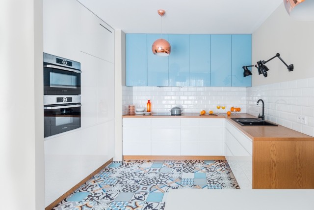Przemyślana aranżacja kuchni - błękit ciągu szafek nad blatem nie jest przypadkowy – dobrze koresponduje z mozaiką na podłodze.