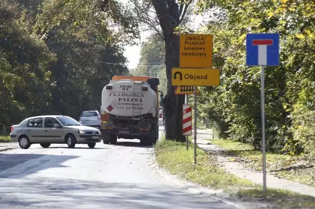 Kierowcy ciężarówek zawracają lub cofają samochody na wąskiej uliczce, prowadzącej do przejazdu kolejowego.