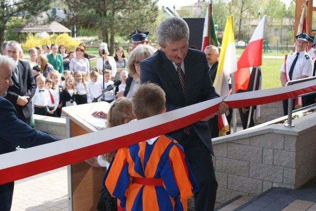 Wójt  Oleśnicy Leszek Juda przecina wstęgę przed wejściem do przedszkola, pomagają mu przedszkolacy.