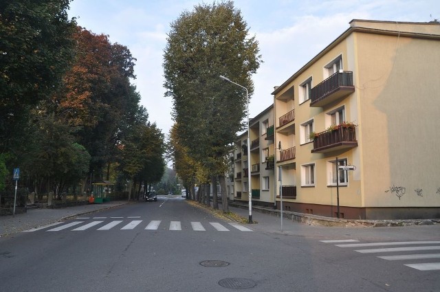 Ulica Powstańców Wielkopolskich, po prawej blok niemal całkowicie zasłonięty przez drzewa. 