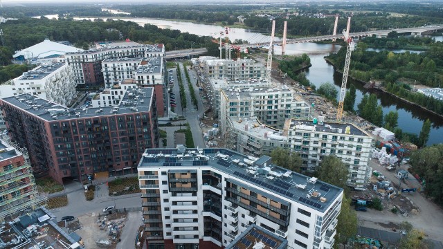 Kolejne budynki Portu Popowice powstają coraz bliżej rzeki. Jakiś czas temu rozpoczął się etap IV tuż przy kanale Odry, gdzie powstające budynki mają już swoją docelową wysokość. Z kolei przy ul. Popowickiej został prawie ukończony 14 kondygnacyjny, jak do tej pory najwyższy zbudowany budynek z całego kompleksu. Ma nawet zamontowane na dachu panele fotowoltaiczne. Do niego ,,przytulone’’ zostały nieco niższe budynki, zawijające w głąb osiedla. Zobacz w galerii zdjęcia z lotu ptaka, jak wyglądają postępy z placu budowy Portu Popowice.