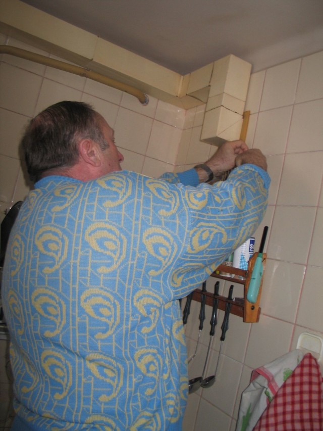 Pan Janusz, jeden z lokatorów szczelnie zakleja kratkę taśmą klejącą, by powietrze z komina nie dostało się do kuchni.