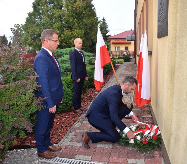 Wieniec z biało-czerwonych kwiatów składa pod tablicą wójt gminy Łukasz Bajgierowicz