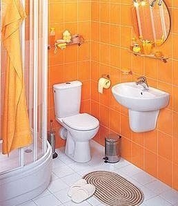 Małą łazienkę powiększają jasne, radosne kafle i powieszone pod kątem lustro.