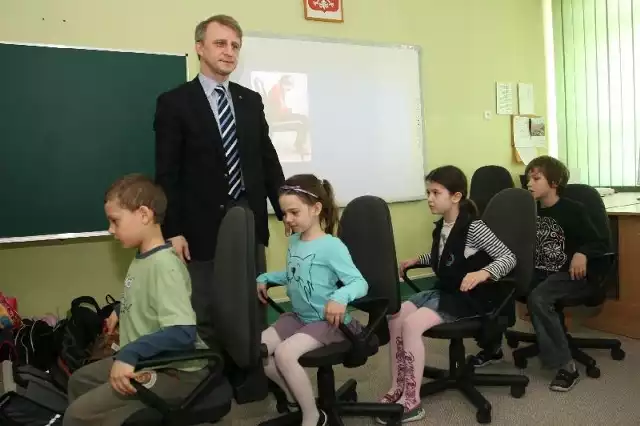 Doktor Wojciech Kiebzak podczas wykładu dla dzieci. Na zdjęciu z lewej postawa przy biurku, która demoluje kręgosłup. Z prawej - podnieś mostek w górę, przesuń miednicę do tyłu i rozluźnij się.