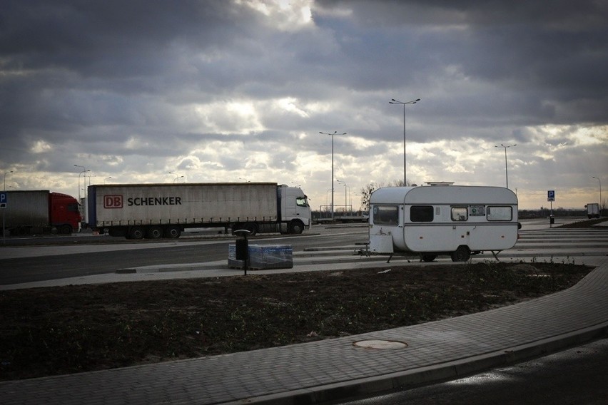 Stróż w zdezelowanej przyczepie pilnuje nowoczesnej drogi i parkingu