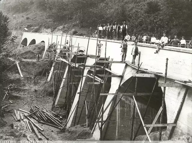 Ponad sto lat temu wykonano to zdjęcie podczas prac nad budową kratownicowego mostu rozpiętego nad rzeką Bóbr, która tutaj wpada do Jeziora Pilchowickiego (jeszcze wtedy w budowie)