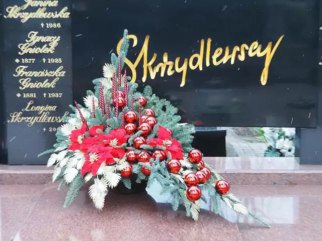 Świąteczny akcent na grobie rodziny Skrzydlewskich to piękny bożonarodzeniowy stroik z czerwonymi bombkami