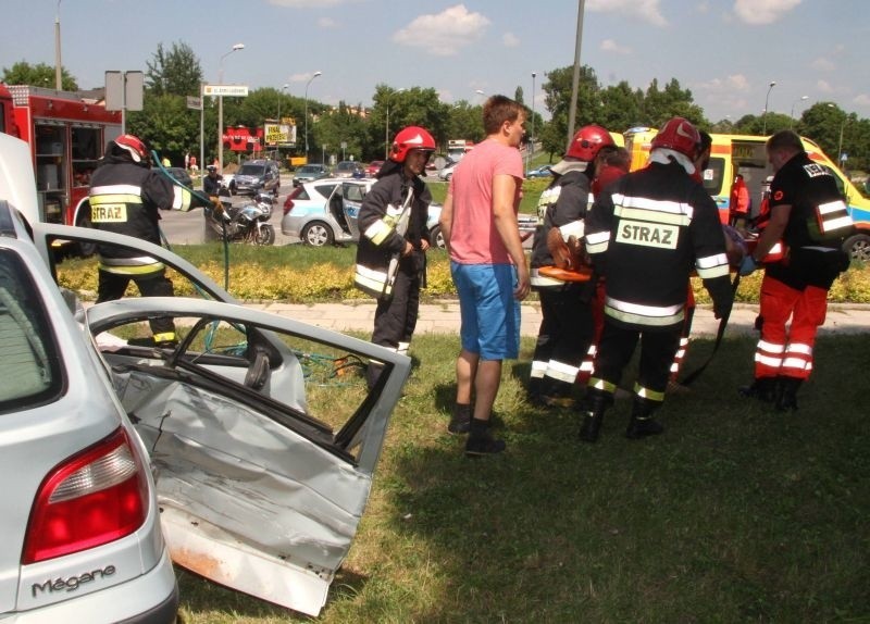 Strażacy niosą do ambulansu pasażerkę renaulta.