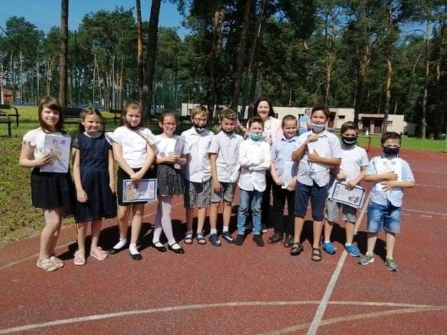 Uczniowie w małych grupach odbierali szkolne świadectwa na boisku szkoły podstawowej numer 2 w Kozienicach.