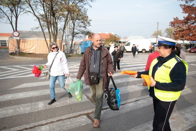 Przed wybranymi cmentarzami na Opolszczyźnie policjanci rozdają opaski i kamizelki odblaskowe ufundowane przez Generalną Dyrekcję Dróg Krajowych i Autostrad oraz Wojewódzki Ośrodek Ruchu Drogowego w Opolu. Na zdjęciu policjantka rozdaje kamizelki odblaskowe przed cmentarzem w Opolu Półwsi.