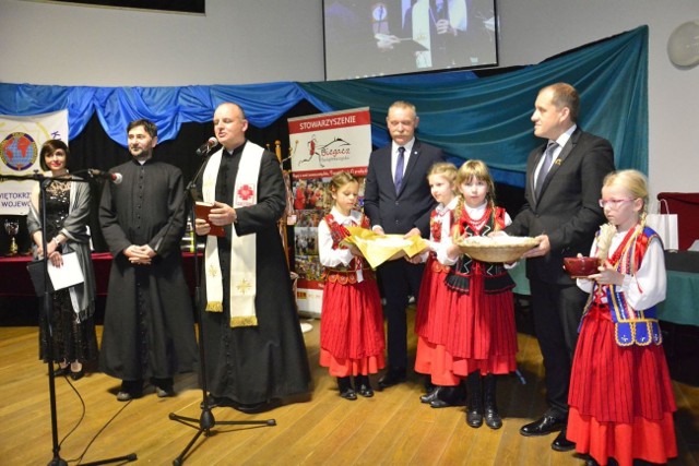 Ksiądz Krzysztof Banasik pobłogosławił opłatek. Pomagały dzieci z Mąchocic Scholasterii, a także gospodarze wieczoru (od prawej) Jacek Wiatrowski i wójt Tomasz Lato.