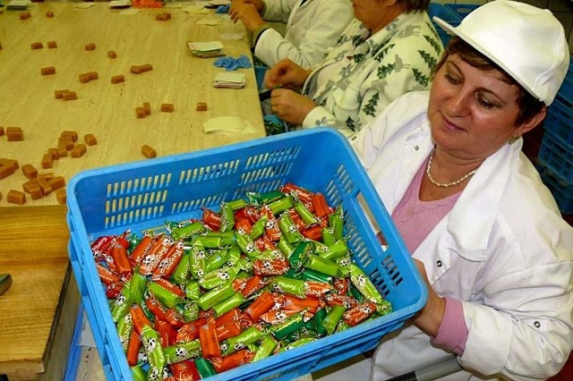 Zawijanie pomadek w dwa papierki &#8211; śliski pergamin i kolorowy papierek z rysunkiem krówek.