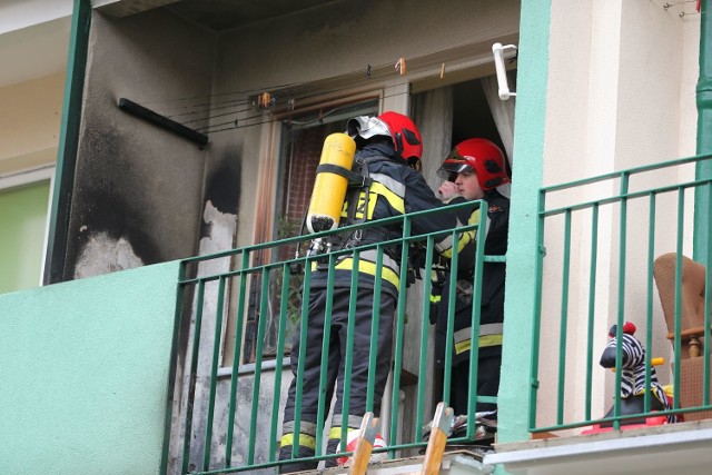 Widać wypalone ściany balkonu na pierwszym piętrze i strażaków dogaszająych pożar.