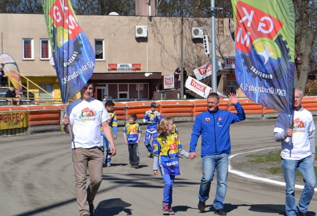 W tle, za ekipą MRGARDEN GKM Grudziądz, widoczne są obiekty hotelu i restauracji Adriano, tuż przy stadionie żużlowym. Na dole siedzibę ma GKM. Na górze jest hotel i lokal gastronomiczny