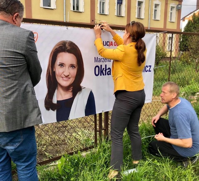 Posłanka Marzena Okła- Drewnowicz wiesza plakaty na ogrodzeniach domostw mieszkańców, którzy się zgłoszą.