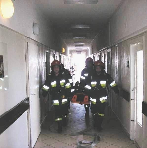 Strażacy wynoszą na noszach poszkodowanego w czasie pożaru pacjenta ze szpitala.