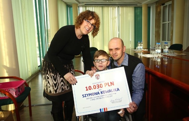 Szymon Kowalik oraz jego rodzice Wioletta i Arkadiusz odebrali w piątek symboliczny czek z pieniędzmi stanowiącymi dochód ze sprzedaży bombek.