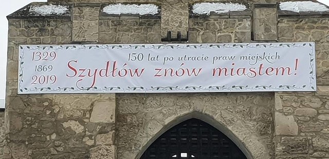 Baner informujący o odzyskaniu praw miejskich na murach Szydłowa