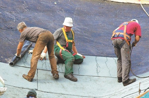 Robotnicy zrywają starą papę z dachu hali. 