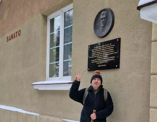 Janusz B. Roszkowski w geście zwycięstwa pod tablicami „Pika”, które wróciły na stare miejsce na frontonie Sanato
