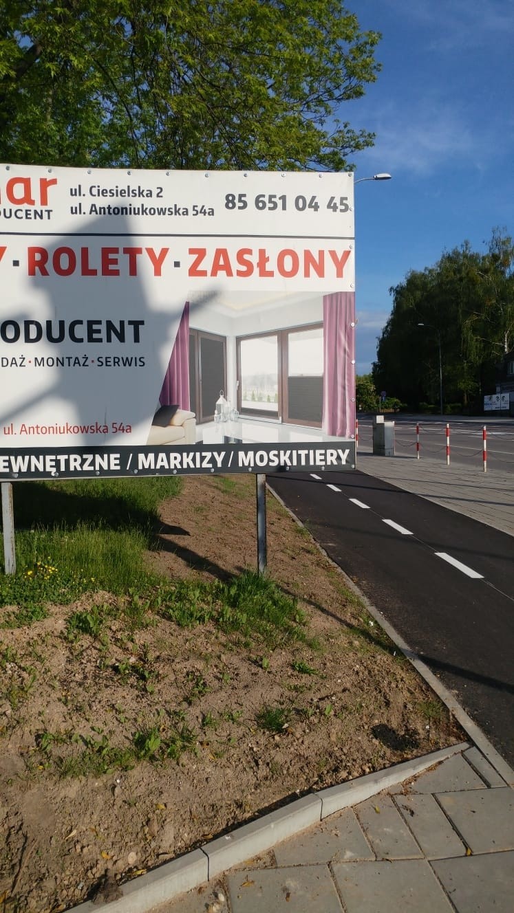 Pędzący rowerzyści chowają się za tablicą reklamową. Piesi...