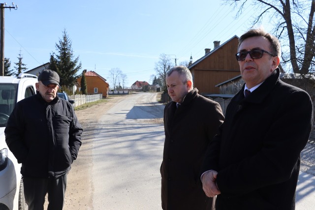 Od prawej strony stoją starosta Dariusz Czechowski, wicestarosta Łukasz Karpiński, radny Antoni Drej. W tle remontowana droga w Olesznie.