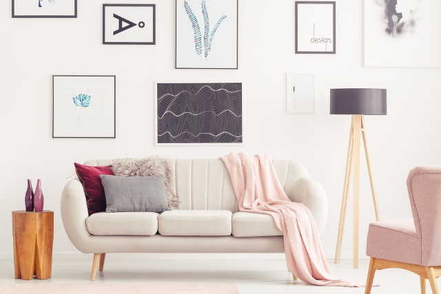 Na zdjęciu kompaktowa sofa na nóżkach w jasnym kolorze oraz fotel i modne dodatki wykończone drewnem w stonowanej kolorystyce.