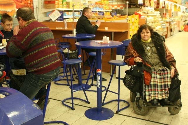 Anna Sowa, pełnomocnik prezydenta ds. osób niepełnosprawnych, pokazuje, że osoba na wózku nie jest w stanie zjeść przy stoliku w Tesco, bo do niego nie dosięgnie.