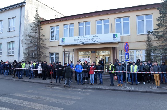 - Ludzie wkładają serce w produkcję sody, a od pół roku nie otrzymują premii motywacyjnej - mówi Jarosław Dąbek, przewodniczący Międzyzakładowego Wolnego Związku Zawodowego Pracowników Produkcji w Ciech Soda Polska w Inowrocławiu. Z inicjatywy związku, pod siedzibą zarządu inowrocławskiego zakładu sodowego odbyła się pikieta. Protestujący przekazali władzom spółki petycję, w której przedstawili swoje warunki. Domagają się wypłaty nagrody w wysokości 1000 zł brutto (a nieponad 400 zł) na każdego pracownika, jako rekompensaty premii. Żądają poprawy sytuacji bytowej, szybkiego wypracowania nowego regulaminu premiowania i wprowadzenia dodatku stażowego. Zażądali też, aby w stosunku do organizatorów i uczestników protestu nie prowadzono działań odwetowych. Tymczasem tuż po rozpoczęciu akcji przedstawiciel zarządu Ciech Soda Polska przypomniał uczestnikom, że pikieta odbywa się z naruszeniem prawa. Protestujących wspierał poseł Paweł Skutecki. - Macie prawo do protestowania. Robicie to pokojowo. Nie zakłócacie porządku. Jeśli spadną na was konsekwencje z powodu udziału w proteście na pewno stanę po waszej stronie - zapewniał poseł. Z dziennikarzami na miejscu rozmawiał Mirosław Kuk, rzecznik prasowy Ciech Soda Polska. W firmie nie udało się wypracować założonych warunków, które umożliwiłyby wypłatę premii. Zarząd zdecydował jednak, że załoga otrzyma nagrody za zaangażowanie w pracę. - Spór powstał na skutek żądań jednego ze związków zawodowych. Chce on wypłaty nagrody w większym wymiarze niż proponuje zarząd. Cztery pozostałe organizacje związkowe zgodziły się na propozycję zarządu - skomentował rzecznik. Otrzymaliśmy stanowisko wspomnianych 4 związków zawodowych, które zaznaczają, że odcinają się od działań prowadzonych przez Międzyzakładowy Wolny Związek Zawodowy Pracowników Produkcji. „(...) Również jesteśmy niezadowoleni z wysokości wynagrodzeń naszych Pracowników, ale drogą dialogu dążymy do poprawienia sytuacji materialnej naszej Załogi. (...) Takim przykładem jest ostateczne uzgodnienie, przez wszystkie organizacje związkowe, wysokości nagrody za zaangażowanie pracowników w pracę za IV kwartał 2018 roku, kiedy to ze względu na brak możliwości wypłaty premii regulowanej, Pracodawca po długich negocjacjach (...) wyraził zgodę na wypłacenie dodatkowej nagrody”. Protest pod siedzibą zarządu Ciech Soda Polska