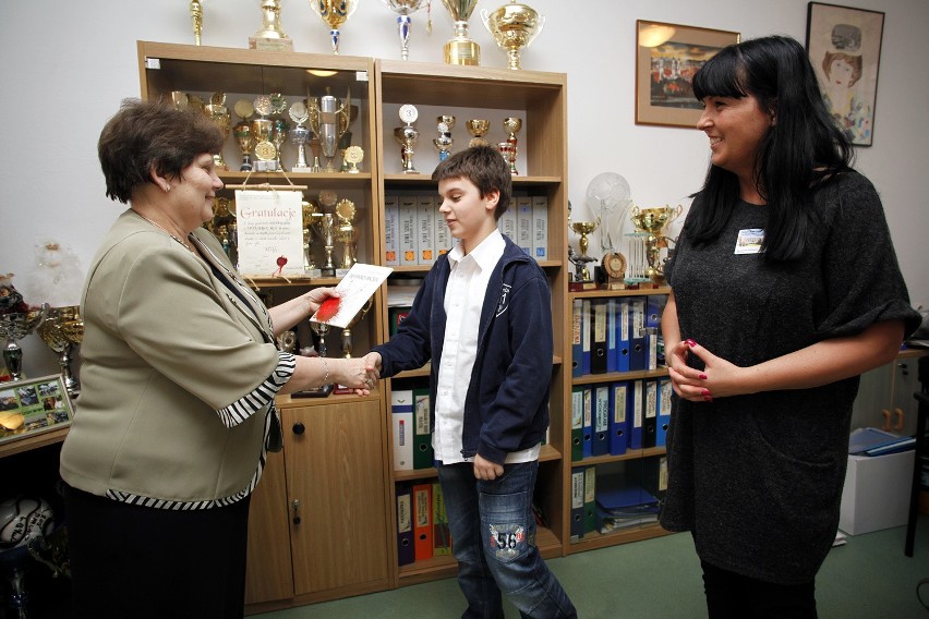 Dyrektor szkoły, Irena Lewandowska, wręcza Michałowi wydany...